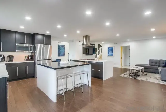 a kitchen with stainless steel appliances granite countertop a sink a stove a refrigerator and white cabinets with wooden floor