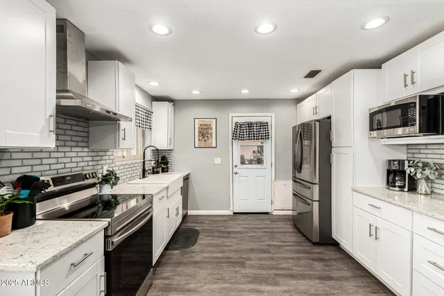 a kitchen with stainless steel appliances kitchen island granite countertop a refrigerator a stove top oven a sink dishwasher and wooden floor