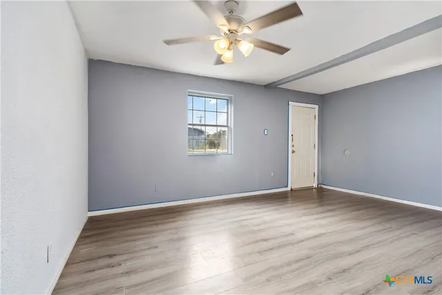 an empty room with wooden floor chandelier fan and windows