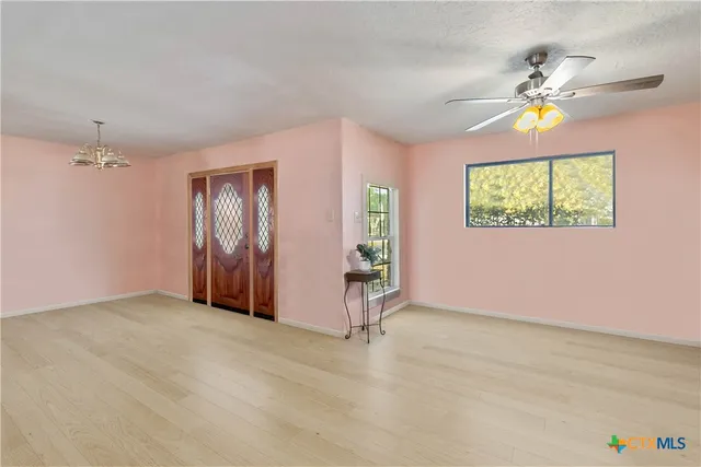 an empty room with windows and chandelier fan