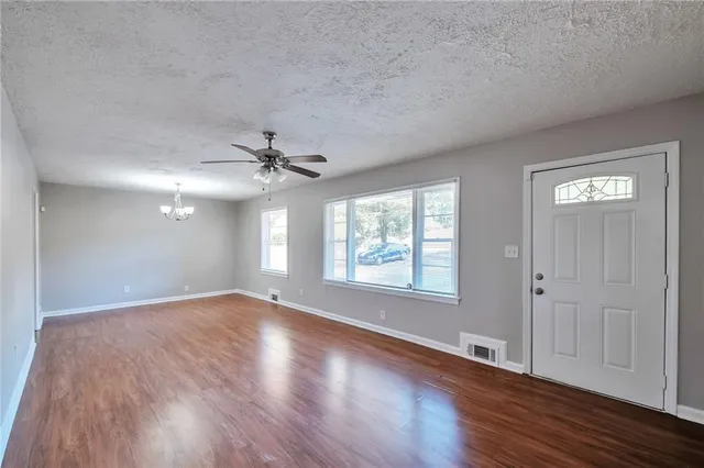 an empty room with wooden floor ceiling fan and windows
