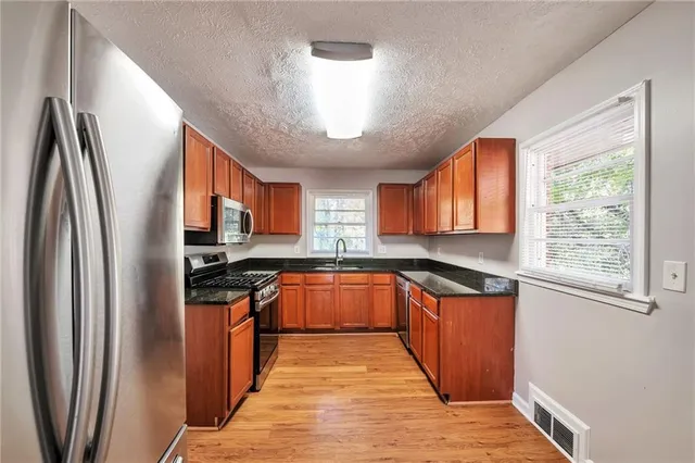 a kitchen with stainless steel appliances granite countertop a refrigerator a sink dishwasher a stove and white countertops with wooden floor