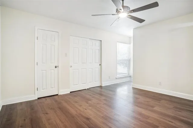 an empty room with wooden floor ceiling fan and windows