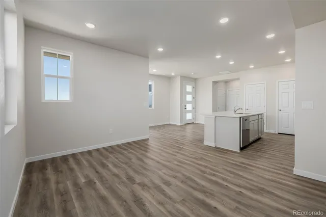 a view of an empty room with wooden floor and a kitchen