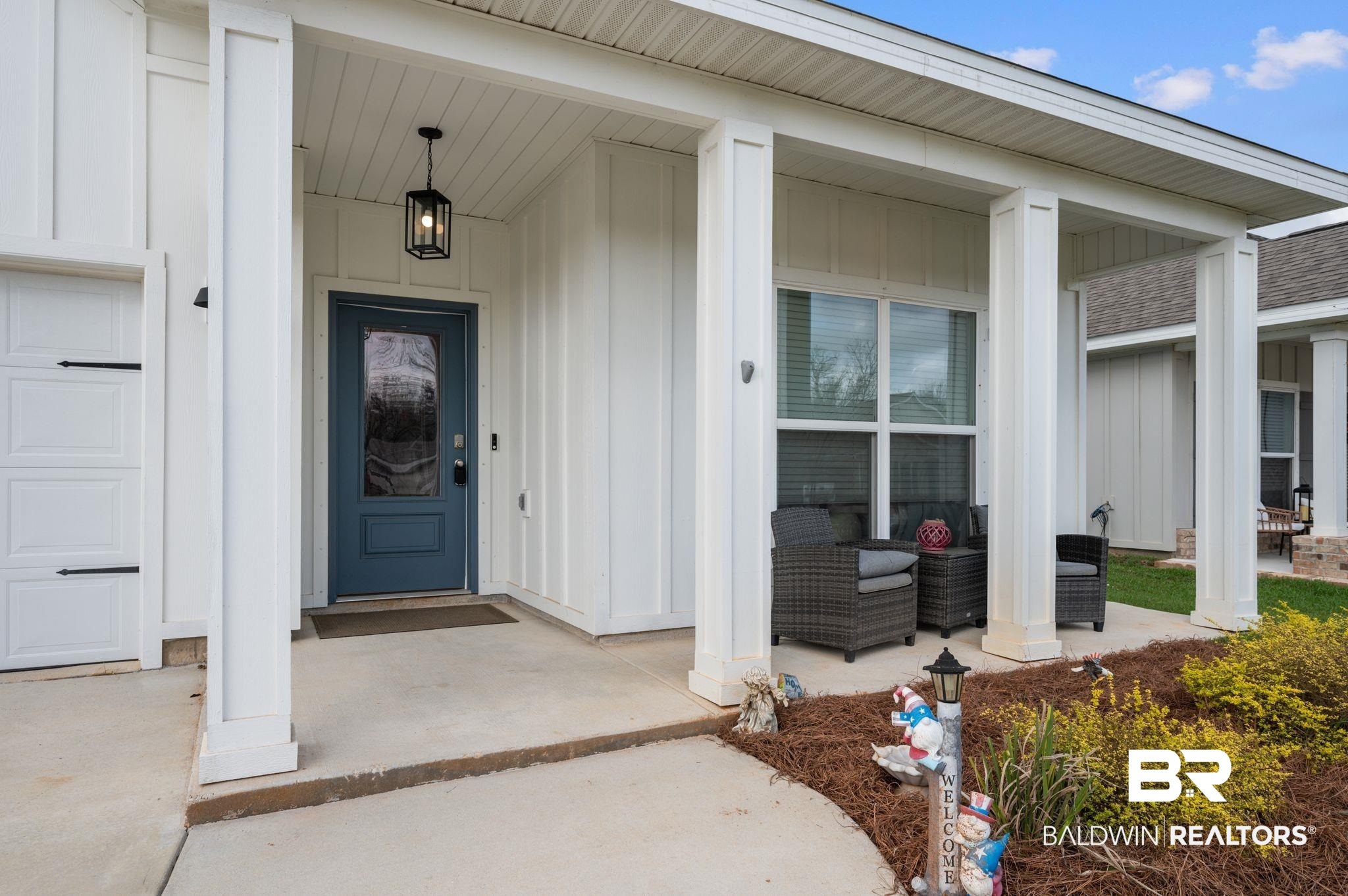 8508 Rosedown Lane Daphne, AL 36526 - Photo 4 of 29 Covered front porch featuring a dark blue entry door with clear glass, board and batten siding, multiple supporting columns, and a concrete walkway