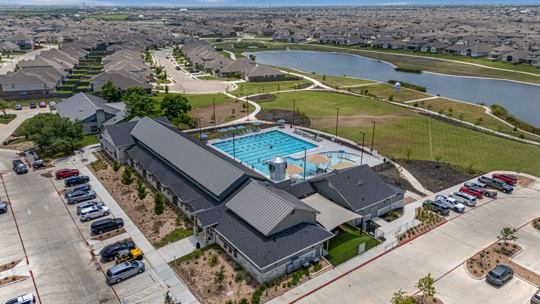 17200 Hope Bergman Road Pflugerville, TX 78660 - Photo 2 of 27 An aerial perspective reveals a vibrant community hub with a sparkling pool and adjacent lake, bordered by rows of neat residences.