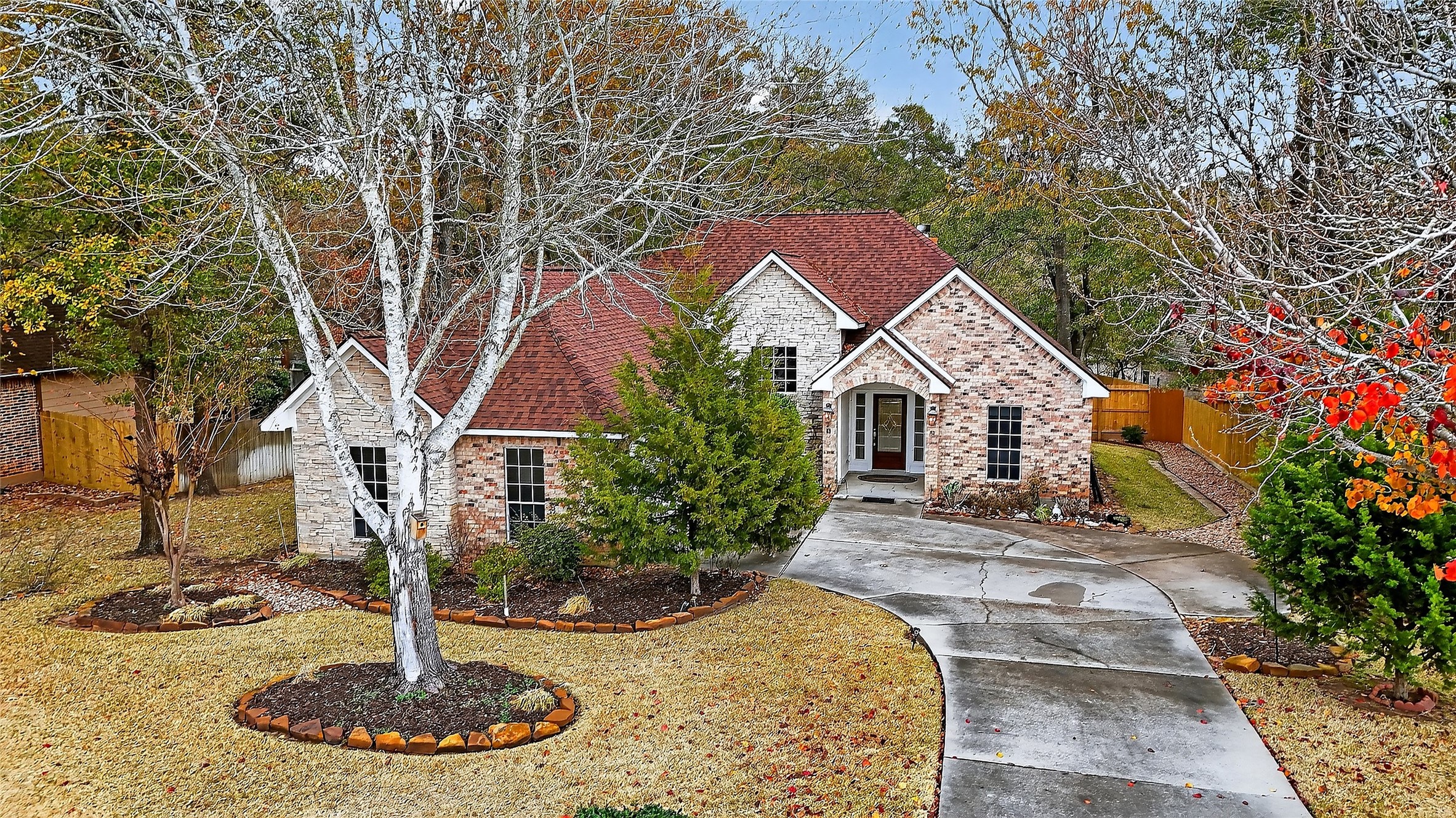 Charming brick façade nestled beneath mature trees, offering inviting curb appeal and a private setting inside the manned gates of April Sound on Lake Conroe.