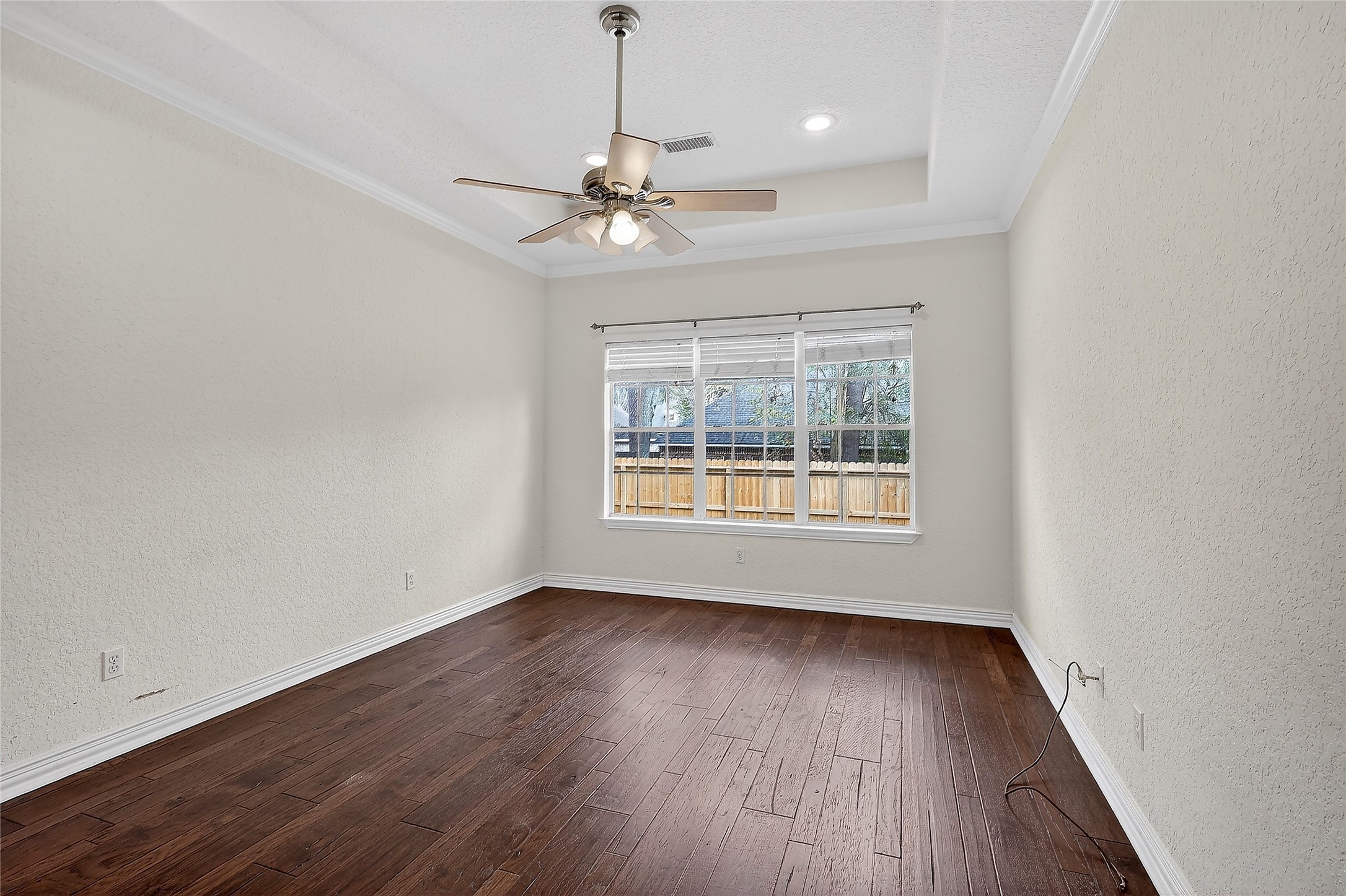 89 Dawns Edge Conroe, TX 77356 - Photo 11 of 46 Spacious primary bedroom featuring tray ceiling detail, rich wood flooring, and large windows overlooking the backyard.