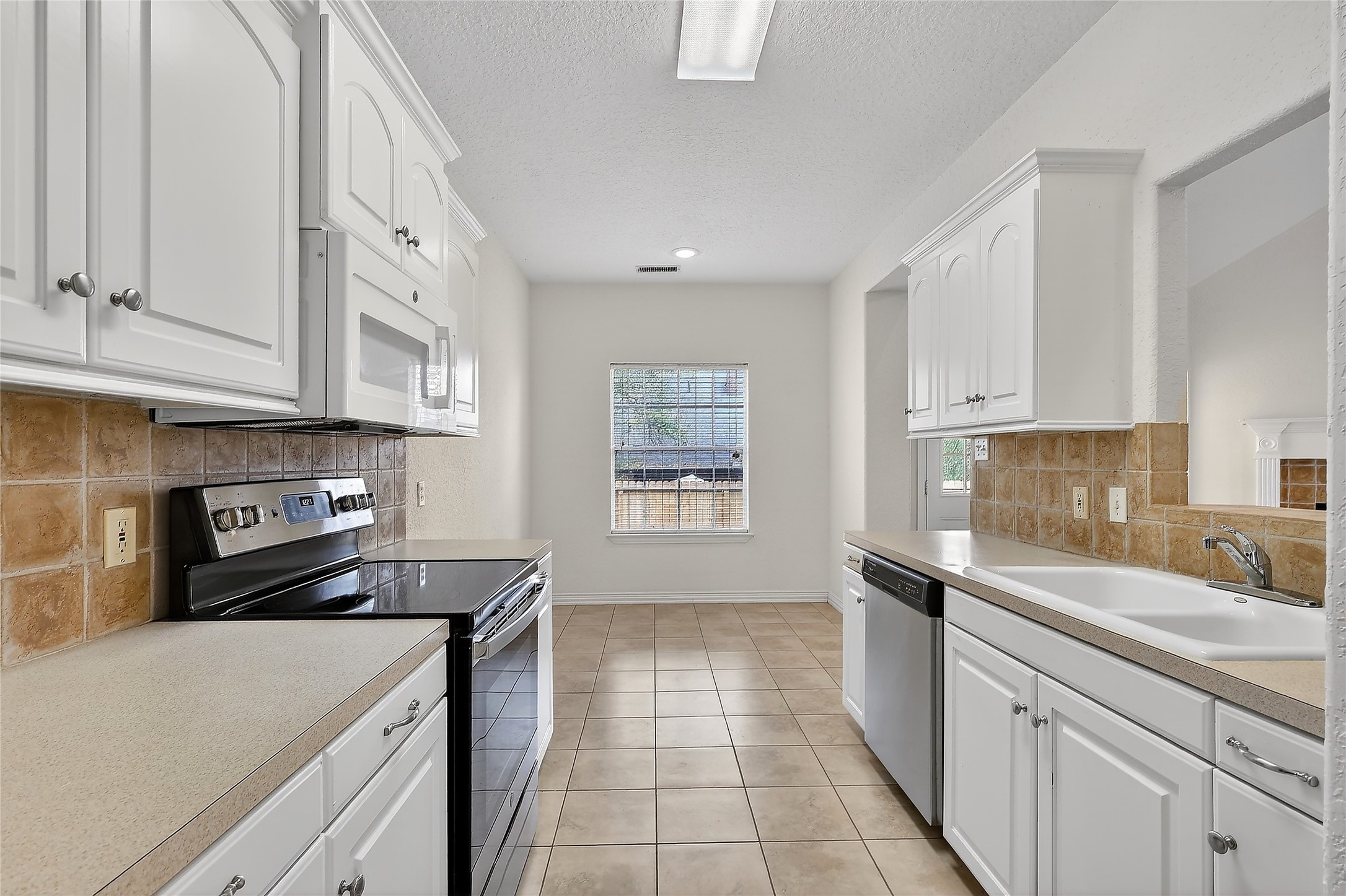 89 Dawns Edge Conroe, TX 77356 - Photo 23 of 46 Efficient galley-style kitchen featuring abundant cabinetry, tile backsplash, modern appliances, and an adjoining breakfast area.