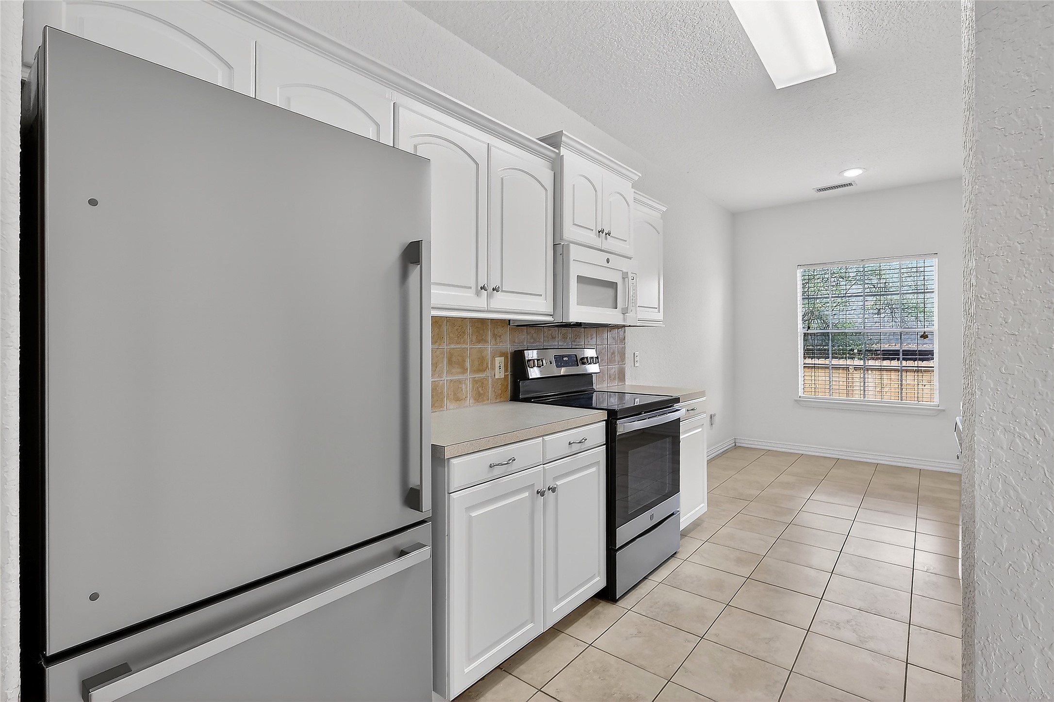 89 Dawns Edge Conroe, TX 77356 - Photo 24 of 46 Well-equipped galley kitchen featuring abundant cabinetry, tile backsplash, modern appliances, and an adjoining breakfast area — kitchen refrigerator conveys.