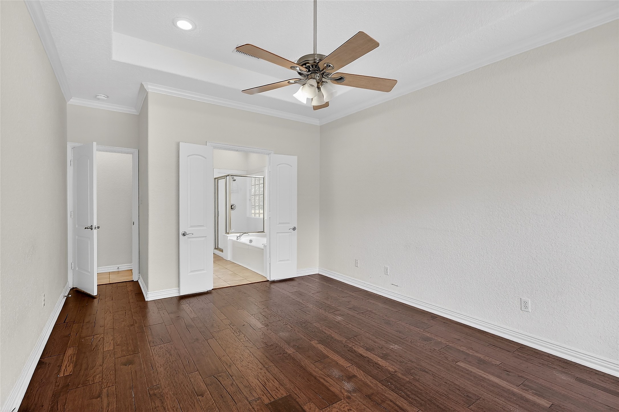 89 Dawns Edge Conroe, TX 77356 - Photo 25 of 46 Primary bedroom showcasing wood flooring, ceiling fan, tray ceiling architecture, and double-door entry into the en-suite bathroom.