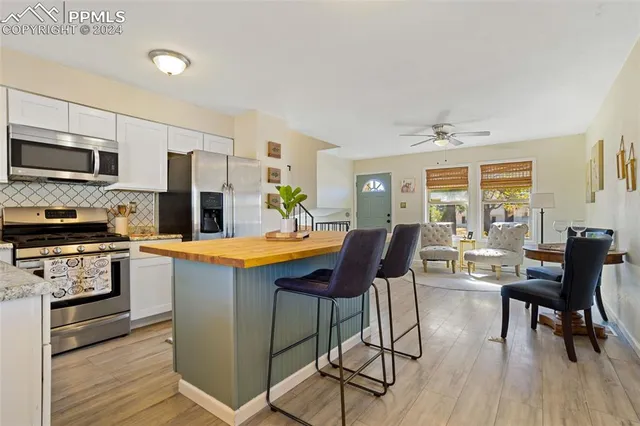 a kitchen with stainless steel appliances granite countertop a stove a refrigerator a kitchen island a dining table and chairs with wooden floor