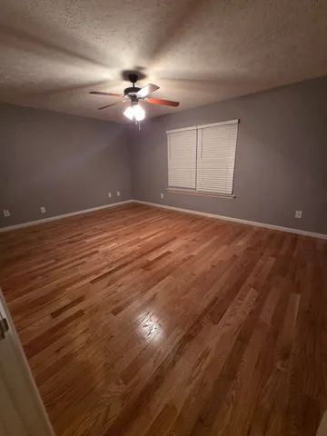 a view of an empty room with wooden floor and a fan