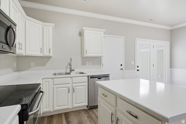 4496 West 11800 South South Jordan, UT 84009 - Photo 10 of 33 Kitchen with stainless steel appliances, ornamental molding, white cabinetry, light wood-style flooring, and a kitchen island