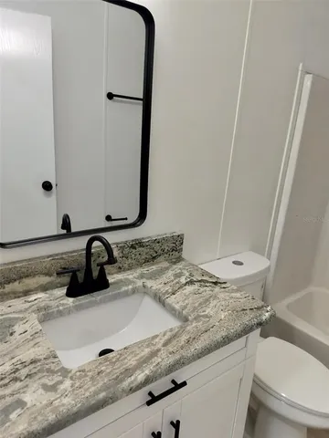 a bathroom with a granite countertop sink toilet and mirror