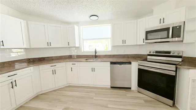 a kitchen with granite countertop white cabinets stainless steel appliances and a sink