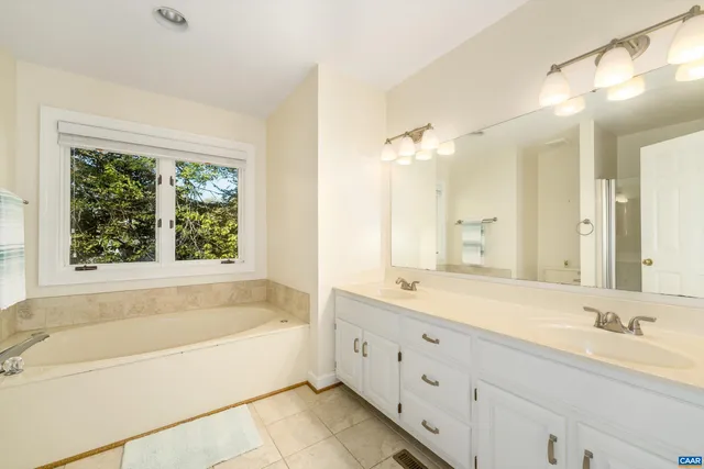 a bathroom with a bathtub a double vanity sink a vanity a window and a shower