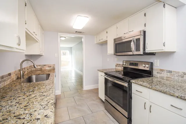 a kitchen with granite countertop a sink stove and cabinets