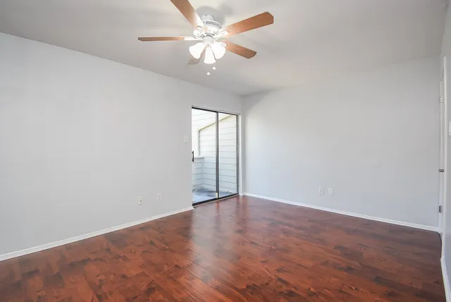 an empty room with wooden floor fan and windows