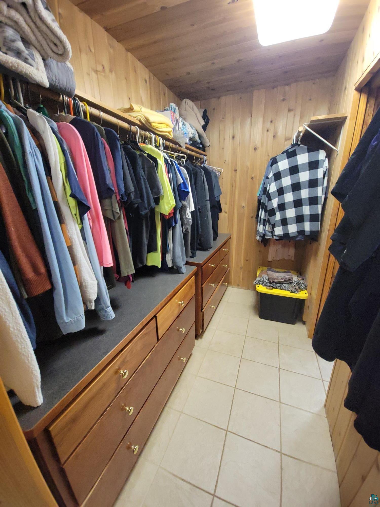 181 Linnell Road Grand Marais, MN 55604 - Photo 54 of 77 Built-in closet system with wood-finish paneling, multiple hanging rods, integrated drawer units, and tile flooring
