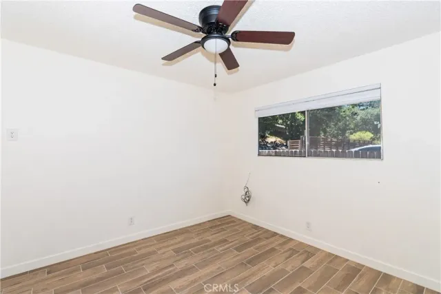 a view of an empty room with wooden floor and a ceiling fan
