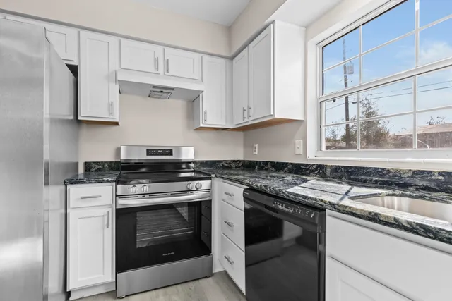 a kitchen with granite countertop a stove top oven a sink and dishwasher a oven with wooden cabinets