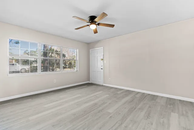an empty room with wooden floor chandelier fan and windows