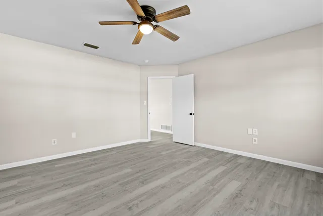 an empty room with wooden floor ceiling fan and window