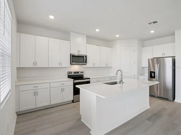 a kitchen with stainless steel appliances granite countertop white cabinets a sink a stove a refrigerator and grey cabinets