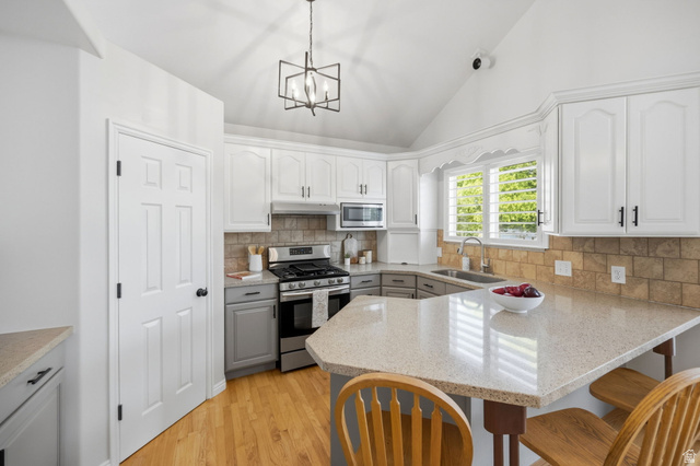 3732 Campbell Road Tooele, UT 84074 - Photo 15 of 69 Kitchen featuring vaulted ceilings, wood-finish flooring, white upper cabinetry, gray lower cabinetry, and a light-toned countertop with an integrated breakfast bar