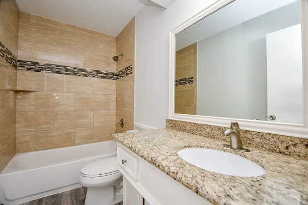 a bathroom with a granite countertop sink toilet mirror and bathtub