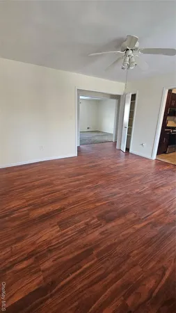 a view of an empty room with wooden floor and a ceiling fan