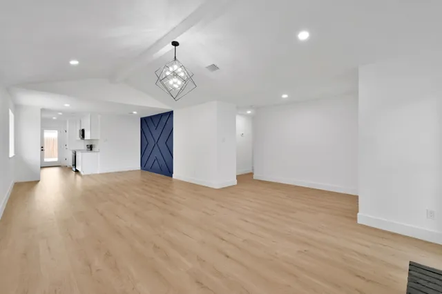 a view of empty room with wooden floor and kitchen view