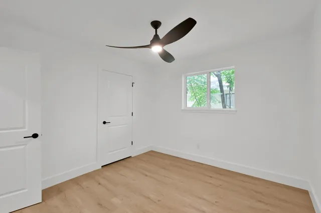 an empty room with wooden floor ceiling fan and windows