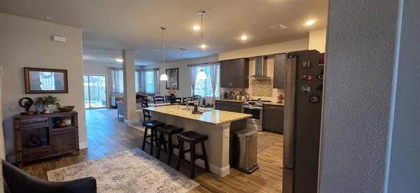 a kitchen with stainless steel appliances granite countertop a refrigerator a sink dishwasher a stove and a dining table with wooden floor