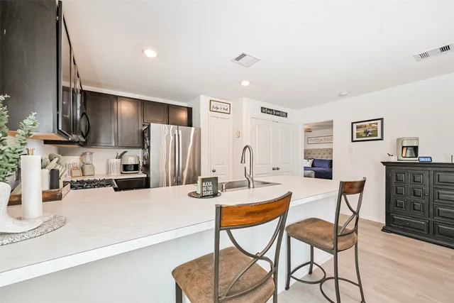 a kitchen with stainless steel appliances kitchen island granite countertop a refrigerator a stove a sink a dining table and chairs with wooden floor