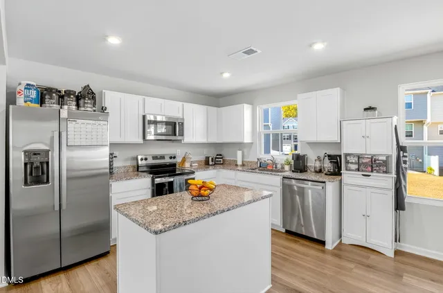 a kitchen with stainless steel appliances granite countertop a refrigerator a stove top oven a sink and dishwasher with wooden floor