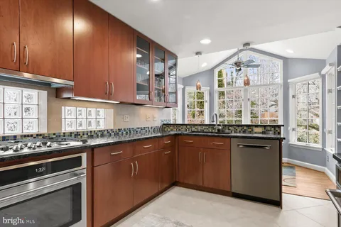 a kitchen with stainless steel appliances granite countertop a refrigerator a sink dishwasher a stove and a dining table with wooden floor