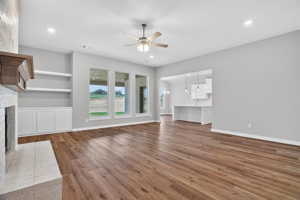504 Clifton Court Springtown, TX 76082 - Photo 6 of 36 Spacious interior with wood-finish flooring, a white brick fireplace with a wood mantle, and built-in shelving with cabinetry