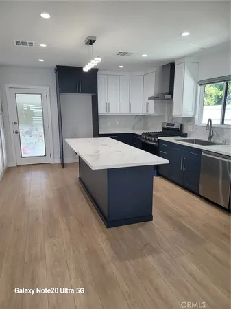 a large kitchen with stainless steel appliances kitchen island granite countertop a sink dishwasher a stove and a refrigerator with wooden floor