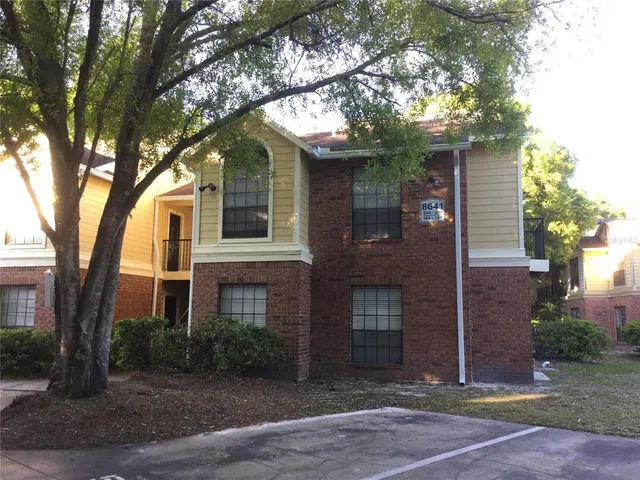 a view of a brick house next to a yard with large trees