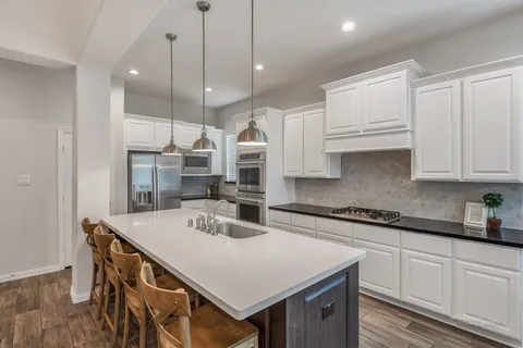 a kitchen that has a lot of cabinets in it with stainless steel appliances granite countertop a stove a sink a refrigerator white cabinets and wooden floor