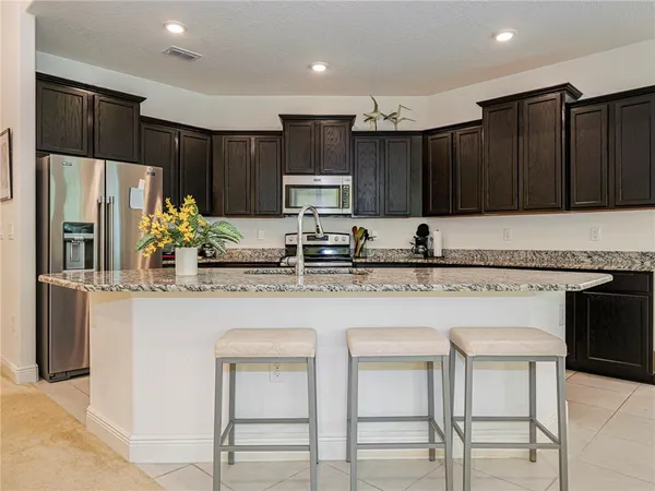 a kitchen with kitchen island granite countertop wooden cabinets a refrigerator a stove a oven and white cabinets