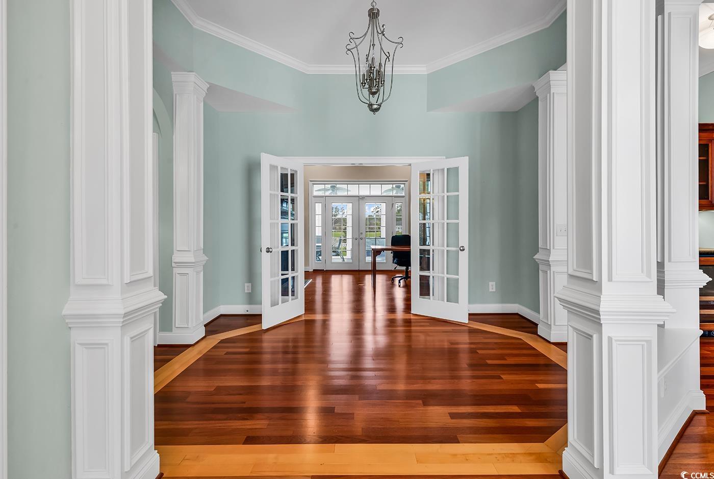 7029 Byrnes Lane Myrtle Beach, SC 29588 - Photo 3 of 40 Unfurnished living area with french doors, hardwood / wood-style flooring, ornamental molding, a chandelier, and decorative columns