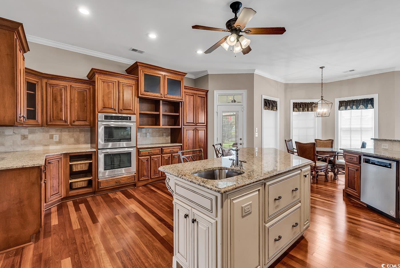 7029 Byrnes Lane Myrtle Beach, SC 29588 - Photo 10 of 40 Kitchen with appliances with stainless steel finishes, brown cabinets, dark wood-style flooring, glass insert cabinets, and crown molding