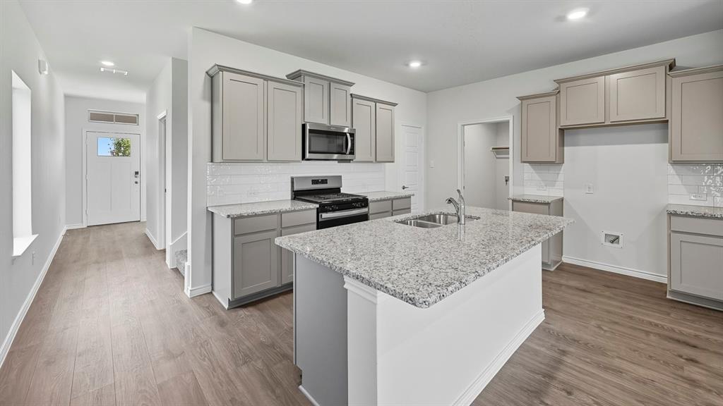 1203 Rusted Rail Drive Princeton, TX 75407 - Photo 23 of 37 Kitchen featuring gray cabinetry, tasteful backsplash, light stone counters, appliances with stainless steel finishes, and an island with sink