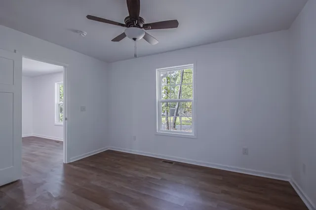 an empty room with wooden floor ceiling fan and windows