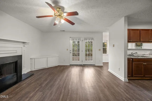 an empty room with wooden floor a ceiling fan a fireplace and windows