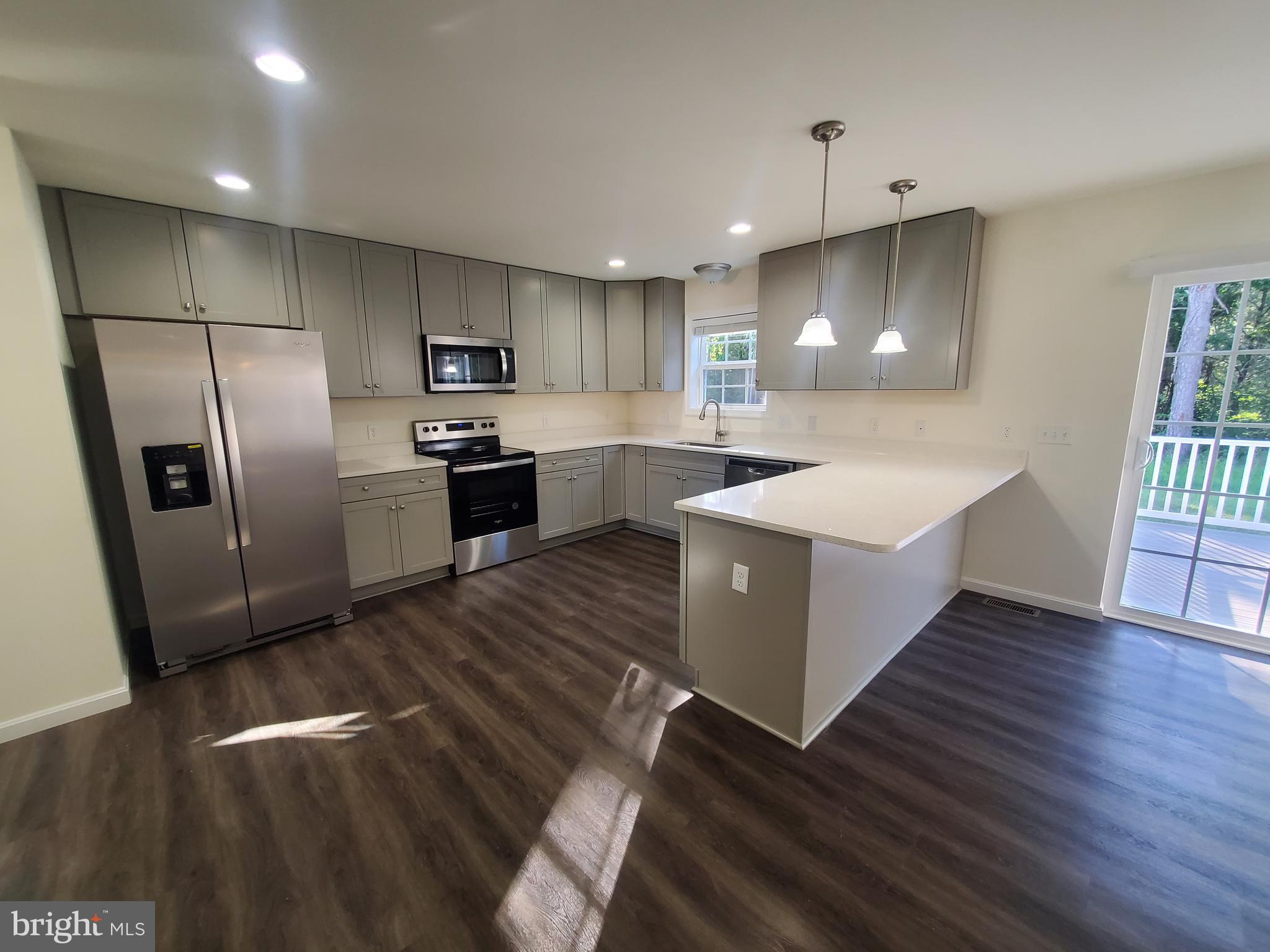 205 Cilento Drive Magnolia, DE 19962 - Photo 28 of 46 a large kitchen with stainless steel appliances kitchen island a sink dishwasher a refrigerator and a stove with wooden floor