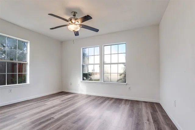 an empty room with wooden floor chandelier fan and windows